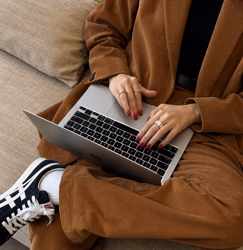 Hands typing on a laptop resting on the lap of someone in a brown suit